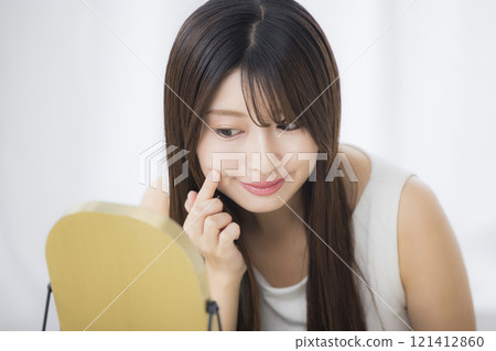 A young woman looks in the mirror and worries about her skin 121412860