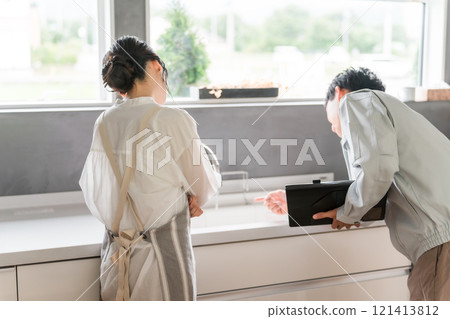 A housewife woman receives explanations from a plumber/equipment shop in the kitchen A housewife woman receives explanations from a plumber/equipment shop in the kitchen 121413812