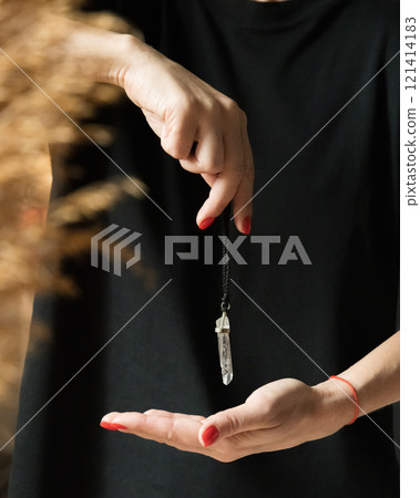 female hands with red nails holding a crystal pendulum on a black thread female hands with red nails holding a crystal pendulum on a black thread 121414183