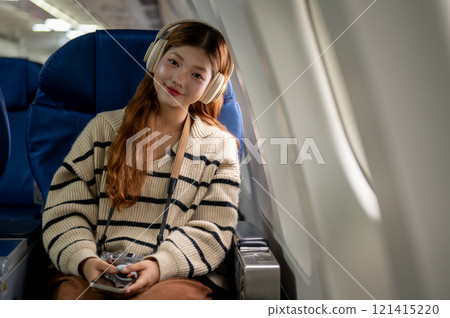 An attractive Asian woman sits at a window seat in the airplane, smiling at the camera. 121415220