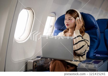 A beautiful woman gazes at the sky view and daydreams while working on her laptop during the flight. A beautiful woman gazes at the sky view and daydreams while working on her laptop during the flight. 121415241