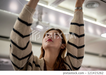 A beautiful Asian woman places her bag in the overhead bin on the airplane, traveling by plane. 121415262