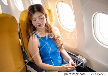 A relaxed and calm Asian female passenger falls asleep while listening to music during the flight. A relaxed and calm Asian female passenger falls asleep while listening to music during the flight. 121415272