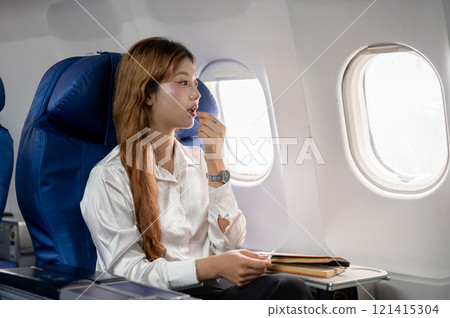 An unwell Asian woman takes airsick medicine during the flight, feeling dizzy, while flying abroad. 121415304