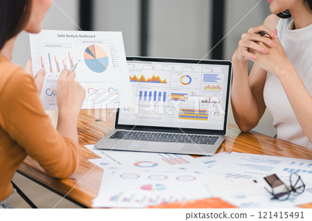 Two colleagues review financial documents with charts and graphs during a business meeting, focusing on analysis and decision-making. Two colleagues review financial documents with charts and graphs during a business meeting, focusing on analysis and decision-making. 121415491