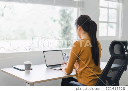 Businesswoman typing on a laptop with a blank screen at a desk in a well-lit home office. Businesswoman typing on a laptop with a blank screen at a desk in a well-lit home office. 121415628