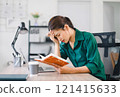 Stressed woman working at home desk, looking at notebook and laptop, managing tasks in home office. 121415633