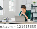 Stressed woman working at home desk, looking at notebook and laptop, managing tasks in home office. 121415635