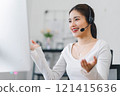 Smiling woman wearing headset, participating in video conference call from home office, using computer for virtual communication. Soft focus 121415636