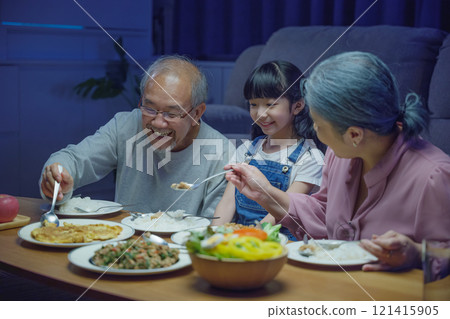 Happy Asian family grandparent and granddaughter dining on table and having fun during at house evening time, Happiness senior parent and child eating dinner food together in living room indoors 121415905