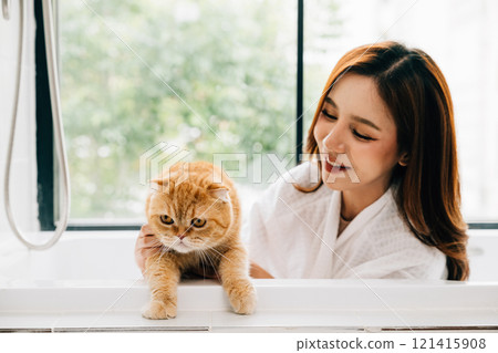 A woman's bathroom retreat includes quality time with her Scottish Fold cat in the tub, portraying the joy of owner-pet love and happiness. A woman's bathroom retreat includes quality time with her Scottish Fold cat in the tub, portraying the joy of owner-pet love and happiness. 121415908
