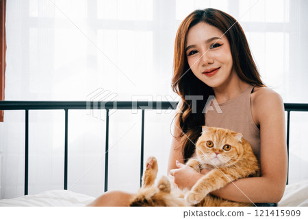 A cheerful woman and her playful Scottish Fold kitten find happiness in each other's company, creating a heartwarming portrait of joy and relaxation in the comfortable bedroom. Pet love A cheerful woman and her playful Scottish Fold kitten find happiness in each other's company, creating a heartwarming portrait of joy and relaxation in the comfortable bedroom. Pet love 121415909