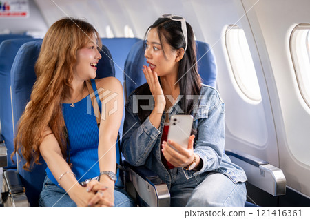 Two happy Asian females traveling on vacation together, enjoying a conversation during the flight. Two happy Asian females traveling on vacation together, enjoying a conversation during the flight. 121416361