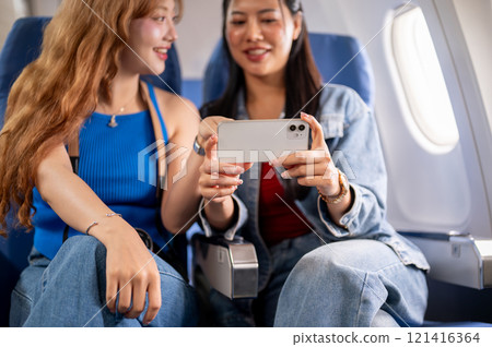 Happy Asian female friends enjoying watching a movie on a smartphone together during the flight. Happy Asian female friends enjoying watching a movie on a smartphone together during the flight. 121416364