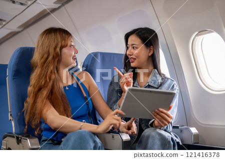 Two cheerful Asian women watch a video on a tablet and enjoy a conversation during the flight. Two cheerful Asian women watch a video on a tablet and enjoy a conversation during the flight. 121416378