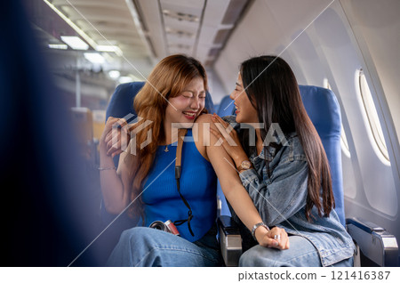 Two joyful Asian female friends, excited for their vacation, sit on a plane with happy expressions. Two joyful Asian female friends, excited for their vacation, sit on a plane with happy expressions. 121416387