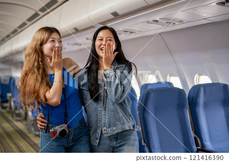Joyful Asian female friends, excited for their vacation, stand at an aisle with happy expressions. 121416390