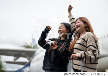 Cheerful Asian female passengers are standing outdoors at the airport, excited for their vacation. Cheerful Asian female passengers are standing outdoors at the airport, excited for their vacation. 121416417
