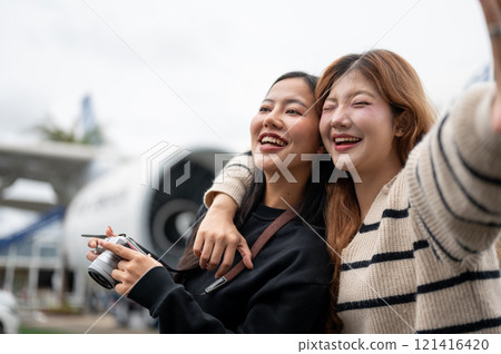 Two female friends, excited for their trip together, are enjoying taking a selfie at the airport. 121416420