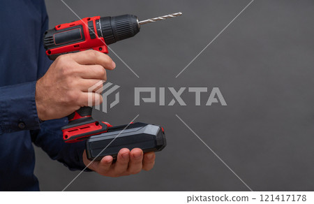 a man installs a battery in a screwdriver. close-up on a gray background. copy space 121417178