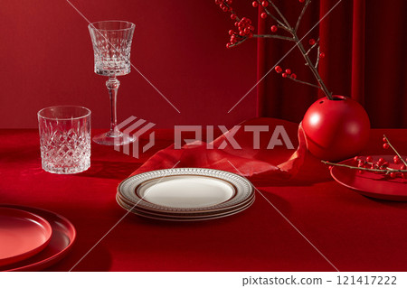 A red new year decoration table was shot from high angle. A stack of white ceramic dish, glasses and some red flower branches displayed on. Blank space for design and adding text 121417222