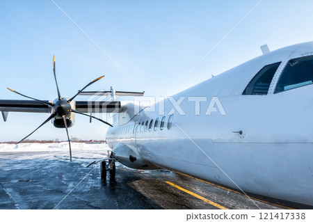 A close-up of the fuselage of a white passenger turboprop airplane on the winter airport apron 121417338