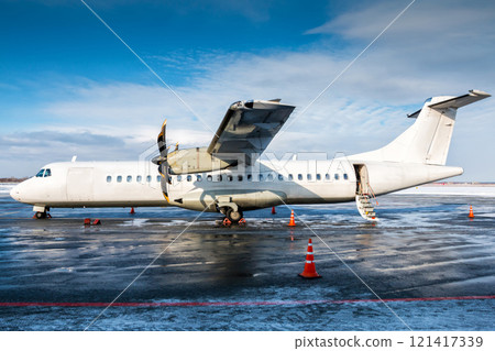 White passenger turboprop aircraft on the apron of the airport with an open staircase ladder in cold winter weather 121417339