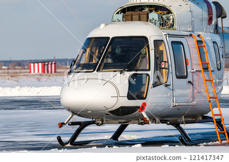 Close-up of a white helicopter with an open engine on the apron of a winter airport Close-up of a white helicopter with an open engine on the apron of a winter airport 121417347