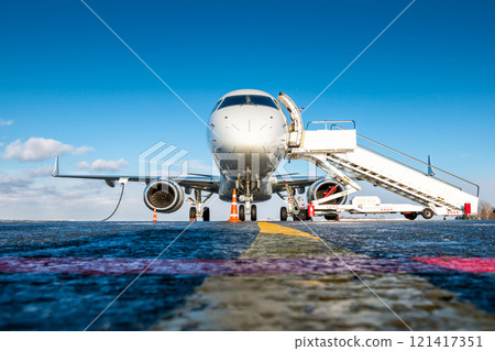Front view of white passenger airplane with a boarding steps at the airport apron 121417351