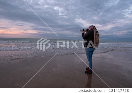A photographer is using a camera to capture the beauty of a sunset on the beach 121417738