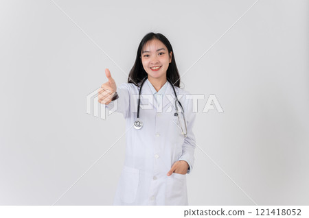 A female doctor stands against a studio background, smiling and giving a thumbs up to the camera. A female doctor stands against a studio background, smiling and giving a thumbs up to the camera. 121418052
