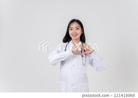 A doctor stands against a white studio background, smiling and making a heart with her hands. A doctor stands against a white studio background, smiling and making a heart with her hands. 121418068