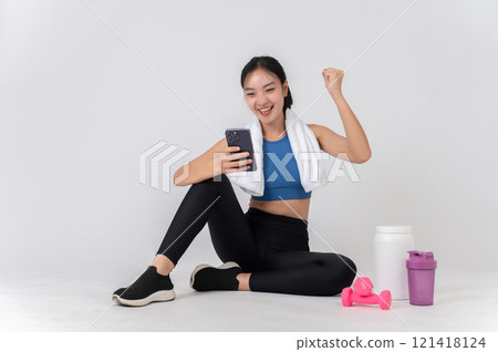 A cheerful woman in sportswear sits on a studio background, raising her triumph fist with excitement A cheerful woman in sportswear sits on a studio background, raising her triumph fist with excitement 121418124
