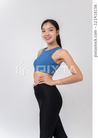 A confident, sporty Asian woman in sportswear smiling at the camera, standing on a studio background A confident, sporty Asian woman in sportswear smiling at the camera, standing on a studio background 121418156