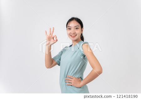 A carefree Asian woman showing her arm with a plaster adhesive bandage and giving a OK hand sign. 121418190