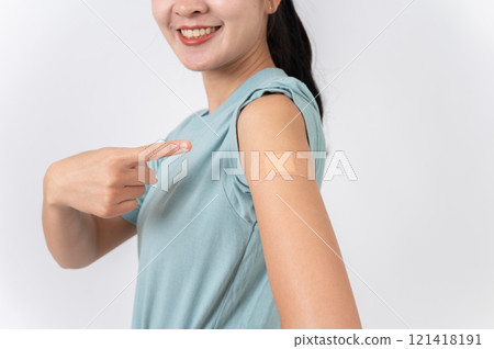 A carefree Asian woman pointing at her arm with a plaster adhesive bandage after getting vaccinated. 121418191