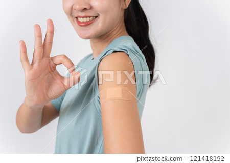 A carefree Asian woman showing her arm with a plaster adhesive bandage and giving a OK hand sign. 121418192