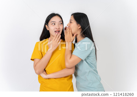 Two Asian female friends whispering a gossip secret to each other, with one amazed by the story. Two Asian female friends whispering a gossip secret to each other, with one amazed by the story. 121418260