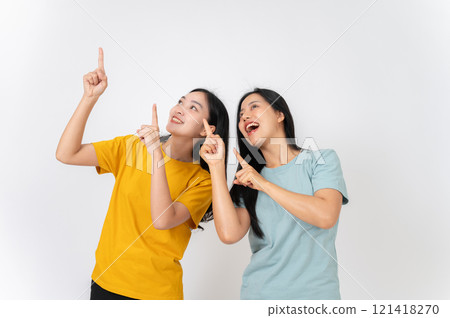 Two cheerful females pointing their finger upward at an empty space, recommending a special offer. 121418270