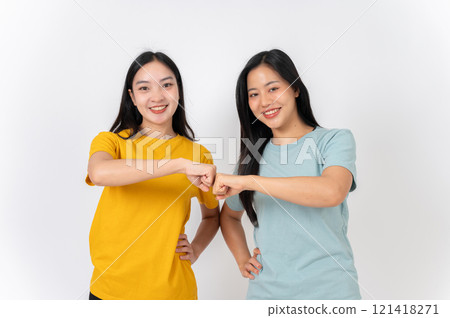 Two young, beautiful Asian female friends doing a fist bump and smiling at the camera. 121418271