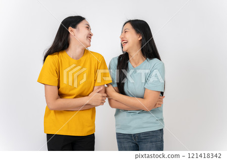 Two cheerful Asian female friends standing on a studio background, enjoying talking and laughing. 121418342