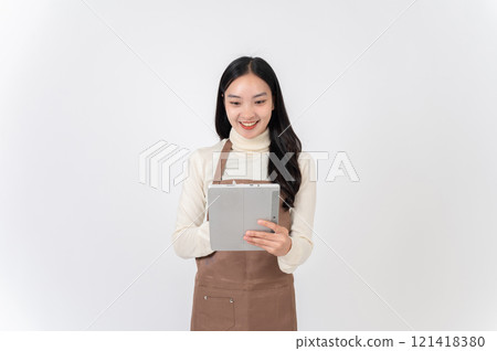A smiling female waitress or coffee shop staff in a brown apron writes order in her digital tablet. 121418380