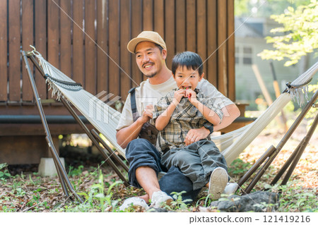 Father and son, boy sitting in hammock at campsite, outdoor leisure 121419216