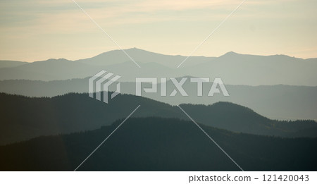 Mesmerizing view of layered mountain ranges in soft shades of green and gray, creating a sense of depth and tranquility under a subtle, misty sky. 121420043