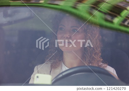 woman with curly hair is seen through the windshield of a car, focusing on driving 121420270