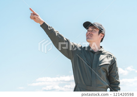 A male worker/mechanic wearing overalls under a blue sky 121420598