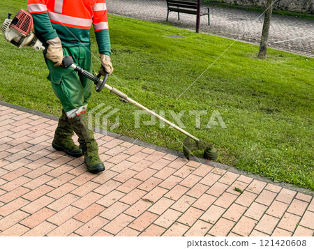 Male worker using trimmer for lawn maintenance in urban park Male worker using trimmer for lawn maintenance in urban park 121420608