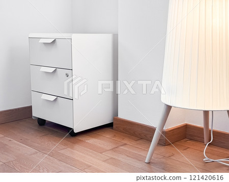 Minimalist white cabinet and modern lamp in bright corner of wooden floored room Minimalist white cabinet and modern lamp in bright corner of wooden floored room 121420616