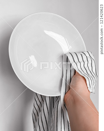 Hand drying white ceramic plate with striped cloth in kitchen setting Hand drying white ceramic plate with striped cloth in kitchen setting 121420623