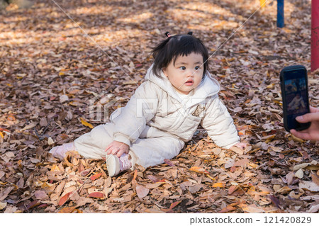 [One-year-old child playing with smartphone in a winter park covered with fallen leaves] 121420829